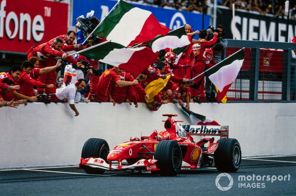 Michael Schumacher, Ferrari F2004, celebrates victory as he crosses the finish line and takes the chequered flag, to the delight of the team who wave Italian flags.